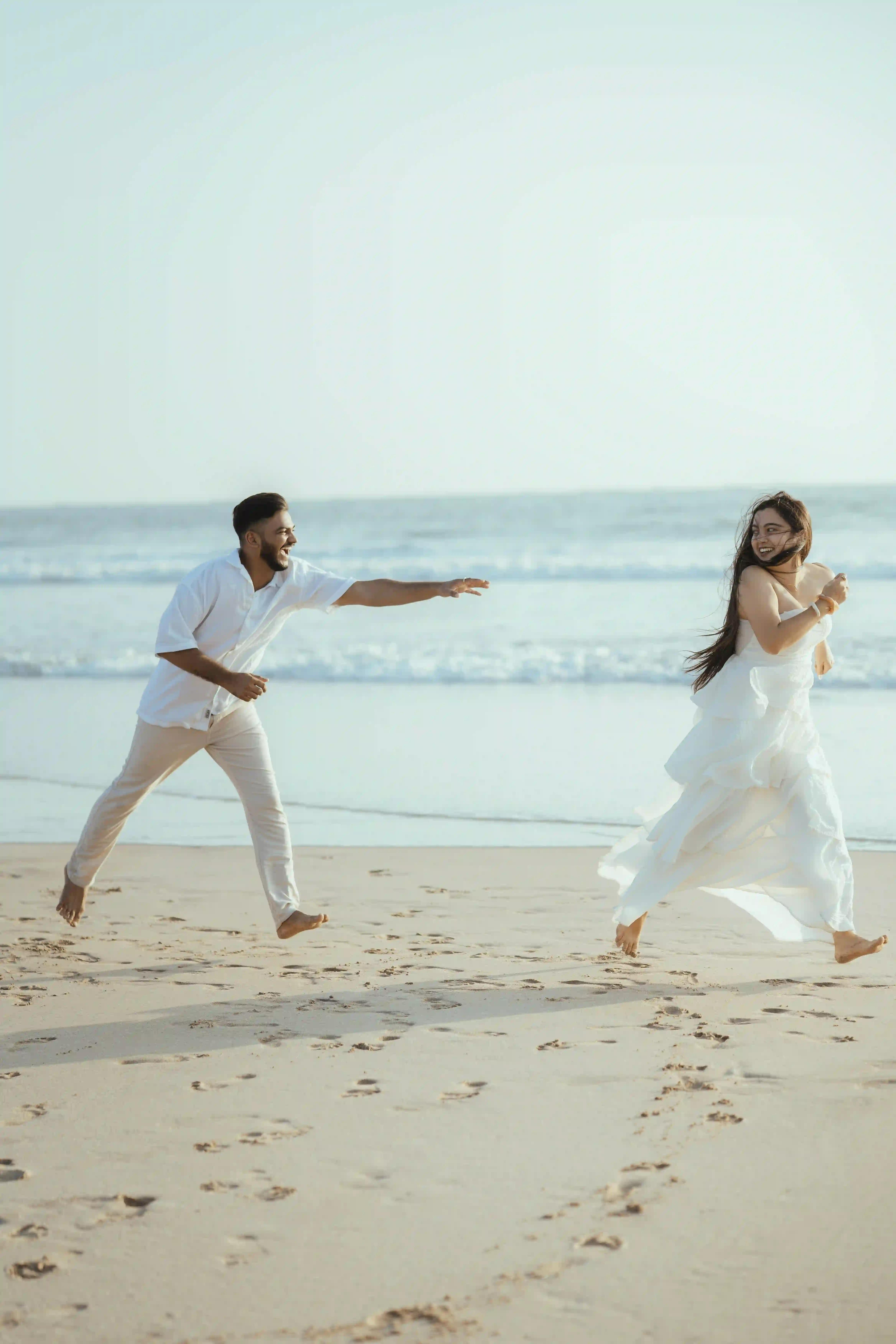 Couple running together on a beach during a pre-wedding photoshoot