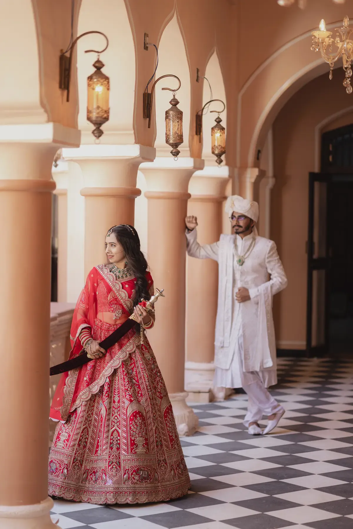 Bride in red bridal lehenga with groom in traditional wedding attire at a heritage venue