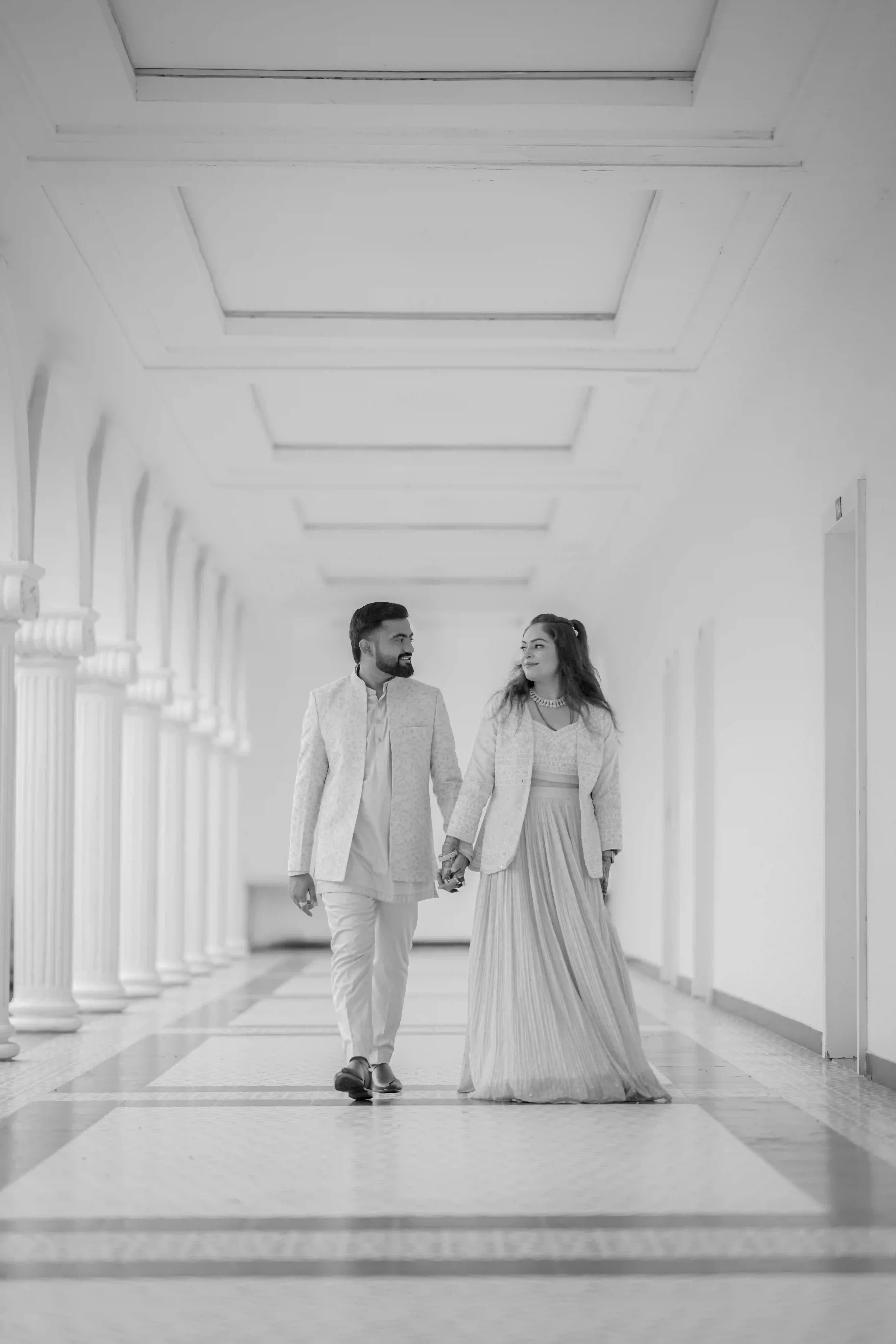 Couple walking hand in hand in traditional wedding attire in a grand corridor